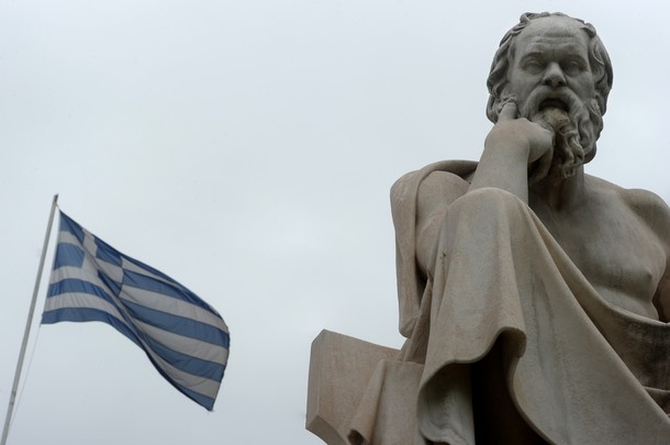 A Greek flag flies next to a statue of a