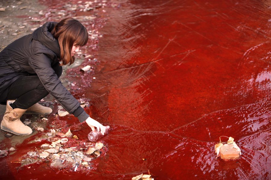 Δημοσιογράφος συλλέγει δείγμα κόκκινου νερού από ένα κινεζικό ποτάμι, πιθανώς μολυσμένου από δύο κοντινά παράνομα εργοστάσια.